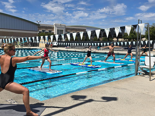 Swan Aquatics - SUP Yoga at Gilroy CHS Aquatic Center - yoga teacher and students in pool on stand-up paddle-boards practicing yoga